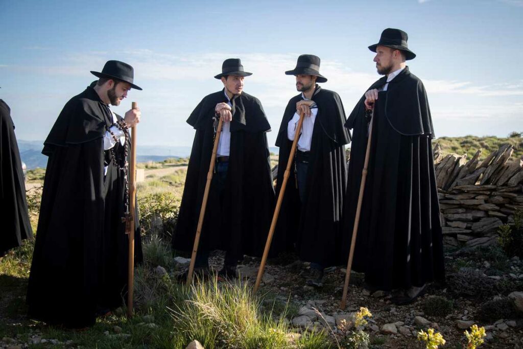 Pelegrins de Portell amb capa negra, barret negre, camisa blanca, rosari i bastó